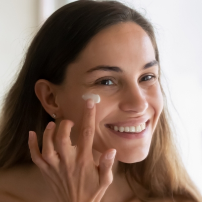 Woman smiling and putting Neora’s Day Cream on her face